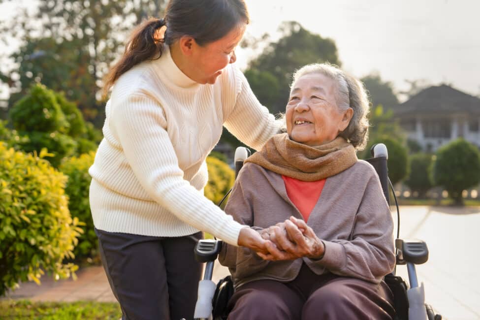closeup happy grandma on wheelchair talking with carer in the garden in the morning sun